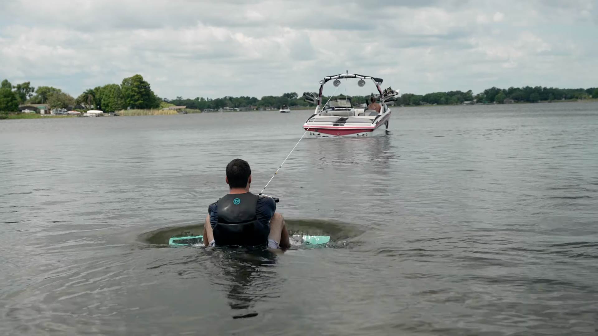 A man in a wet suit is in the water with a wakeboard.