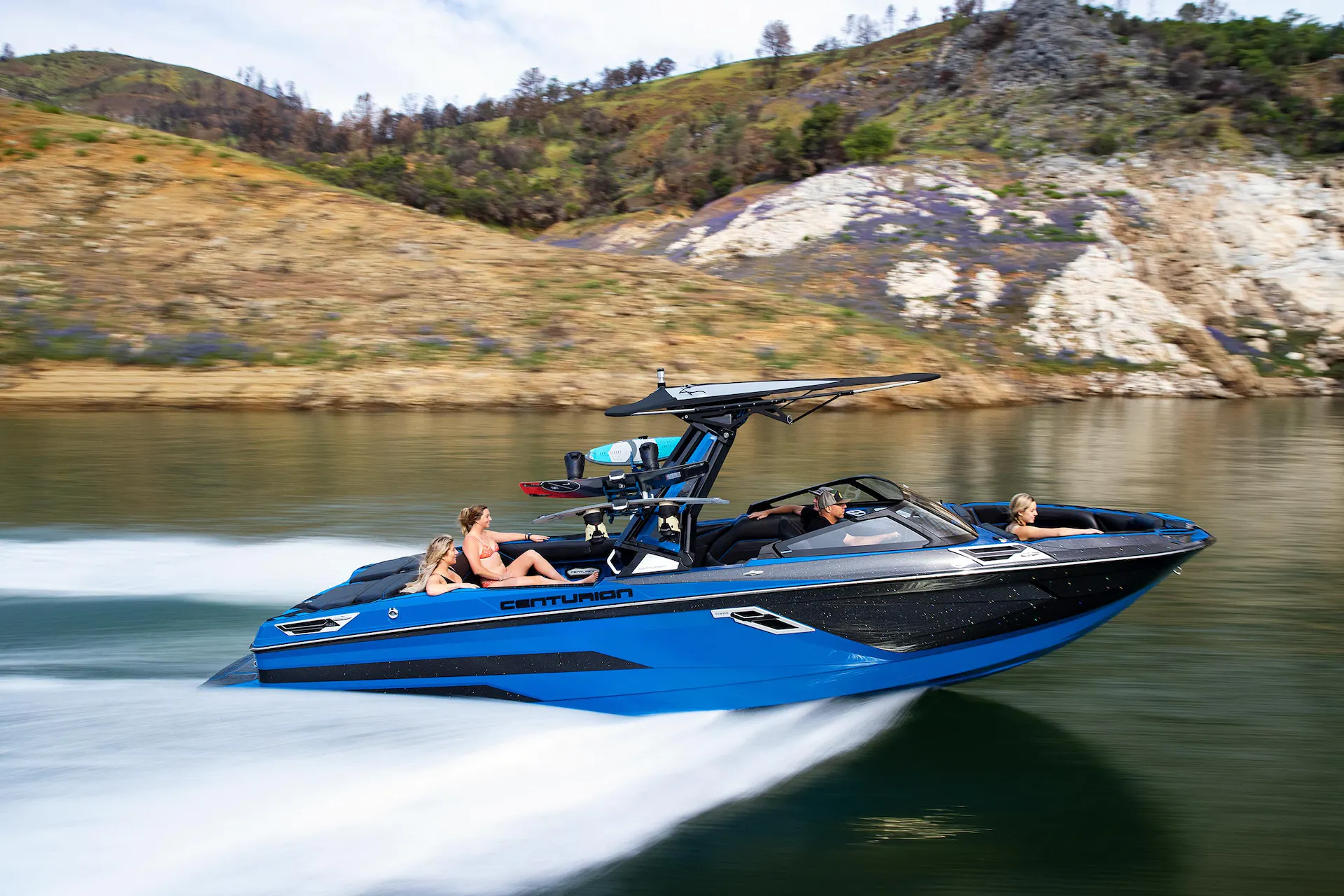 A group of people riding a blue and black wakesurf boat on the water.