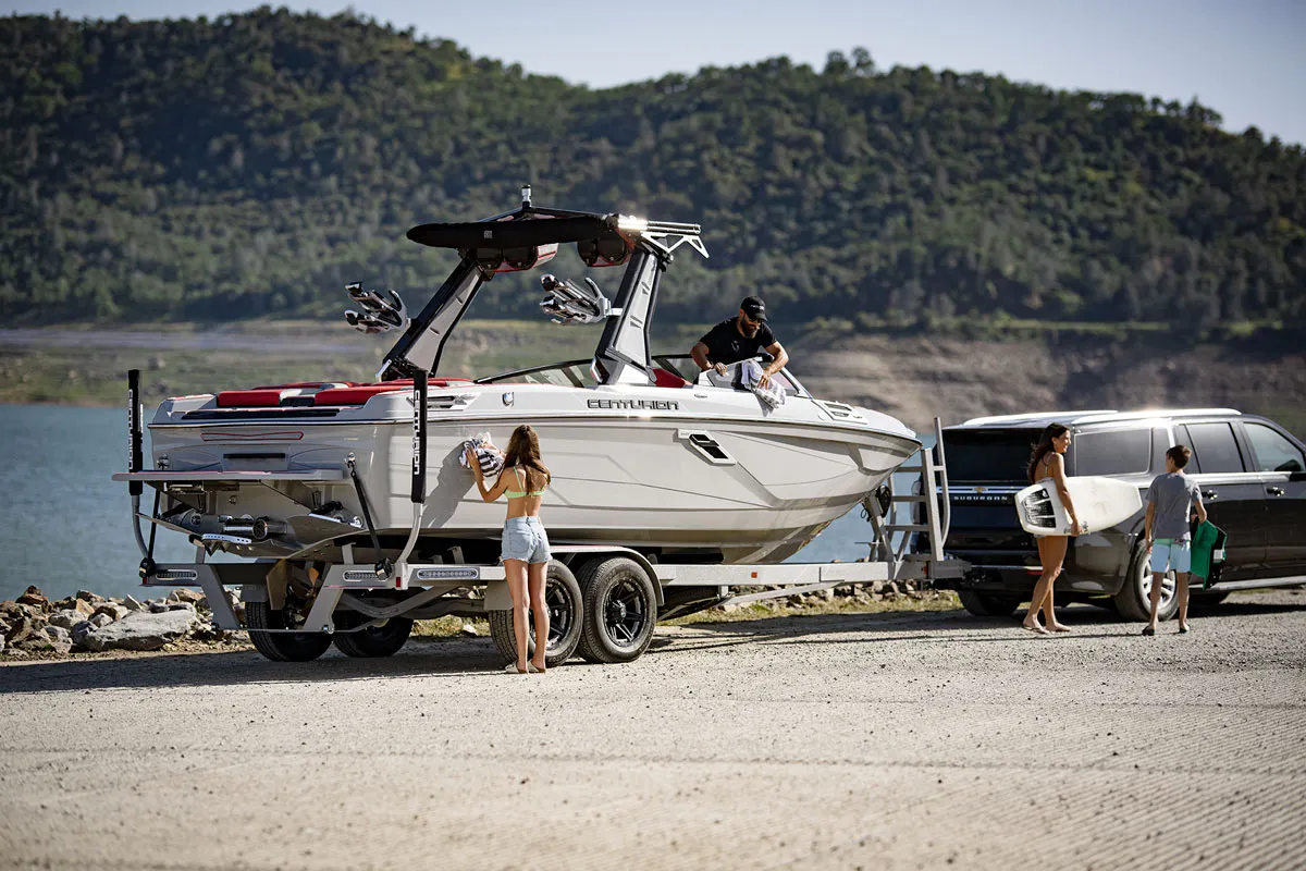 A group of people standing next to a wakesurf boat on a trailer.
