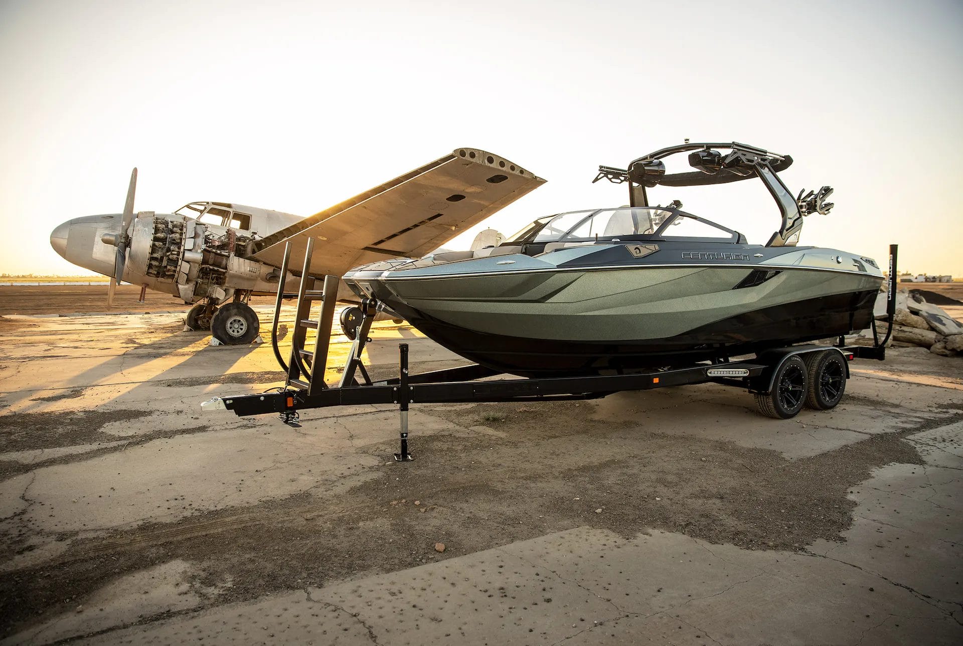 A wakeboat is parked in front of an airplane.