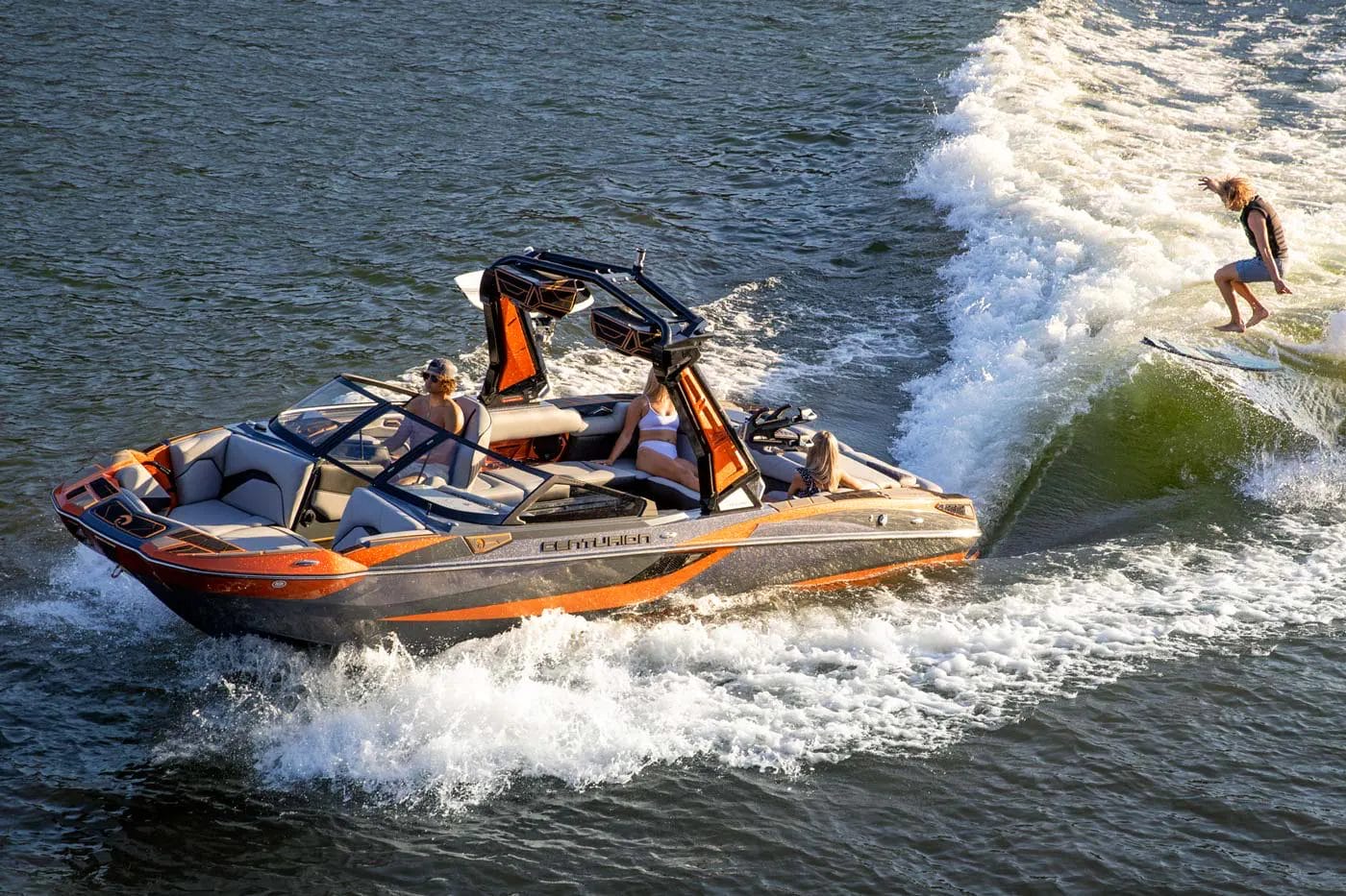 A man is riding a wakeboard behind a wakesurf boat.