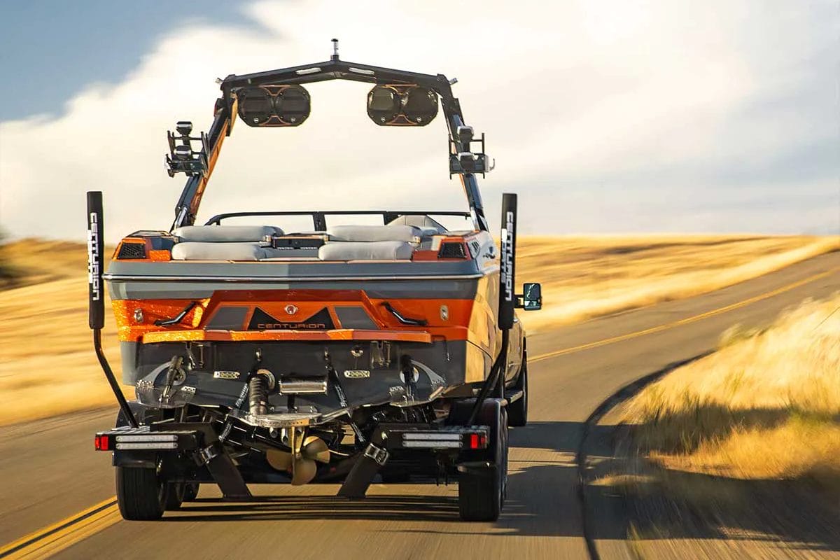 A wakeboat pulling a trailer drives down a country road.