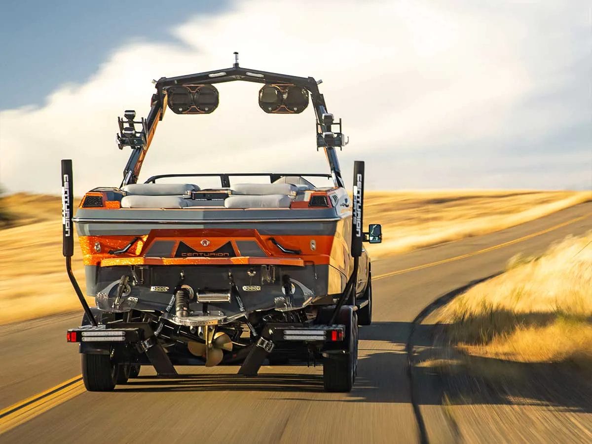 A wakeboat pulling a trailer drives down a country road.