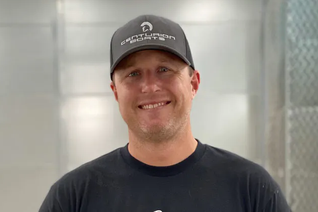 A man wearing a hat and a black shirt while wakesurfing on a wakesurf boat.