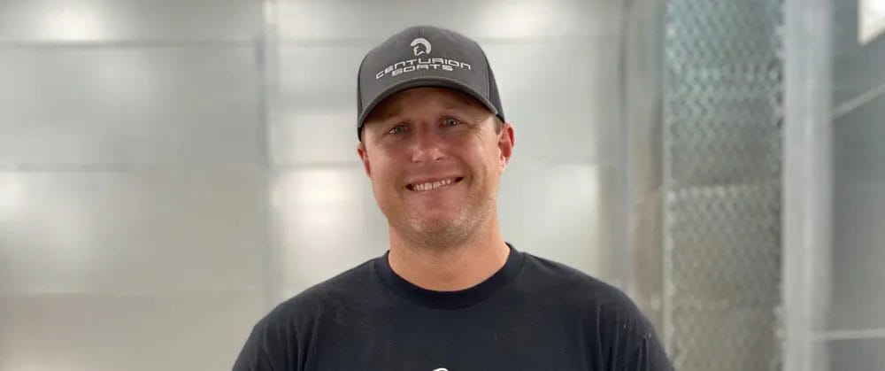 A man wearing a hat and a black shirt while wakesurfing on a wakesurf boat.