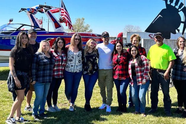 A group of people posing in front of a wakeboat.