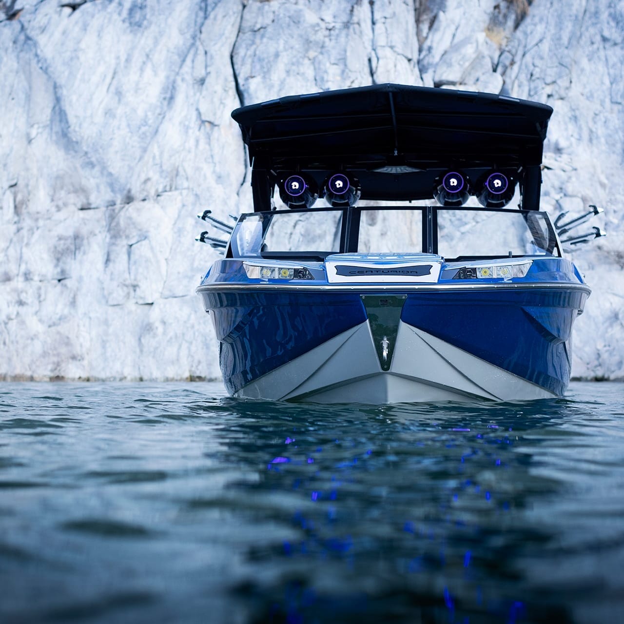 A sleek Centurion Ri230, adorned in blue and white with a black canopy, floats gracefully on the water, framed by the majestic presence of a rocky cliff.