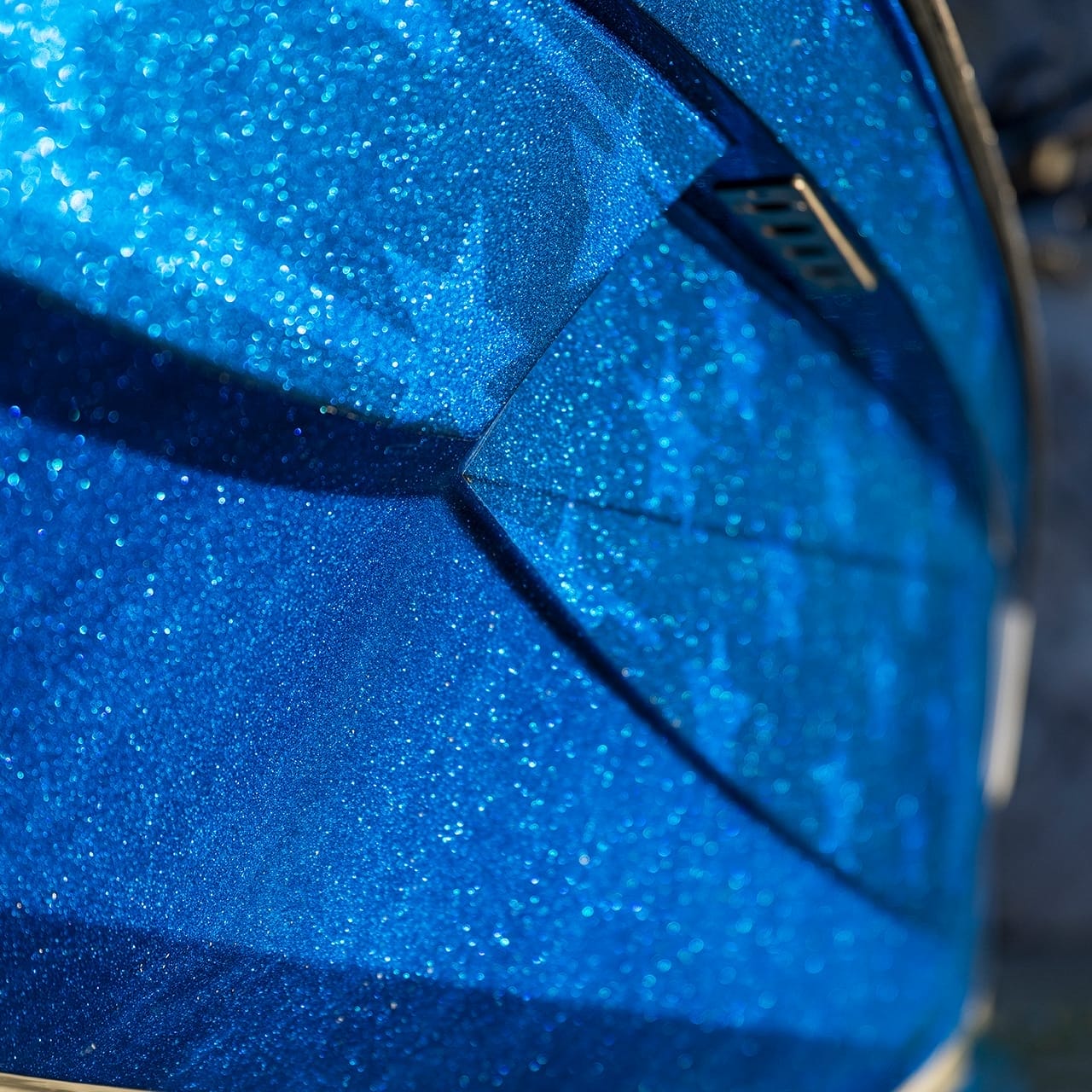 Close-up of a sparkly blue Centurion Ri230 boat surface with geometric shapes and sharp angles, capturing the sunlight in a dazzling display.