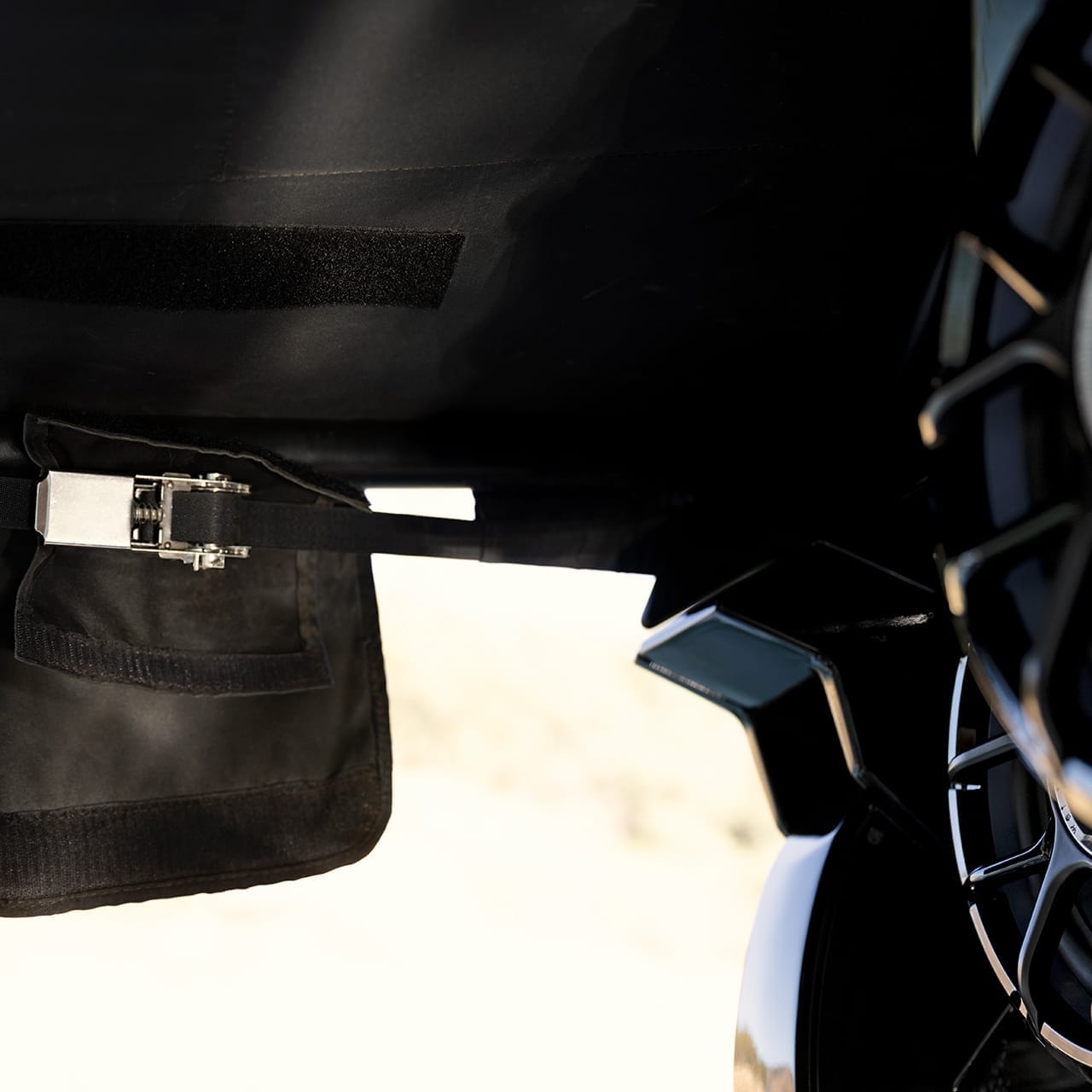 Close-up of a black fabric pouch secured by a strap inside the trunk of a Centurion Ri230. A portion of a black wheel is visible on the right.