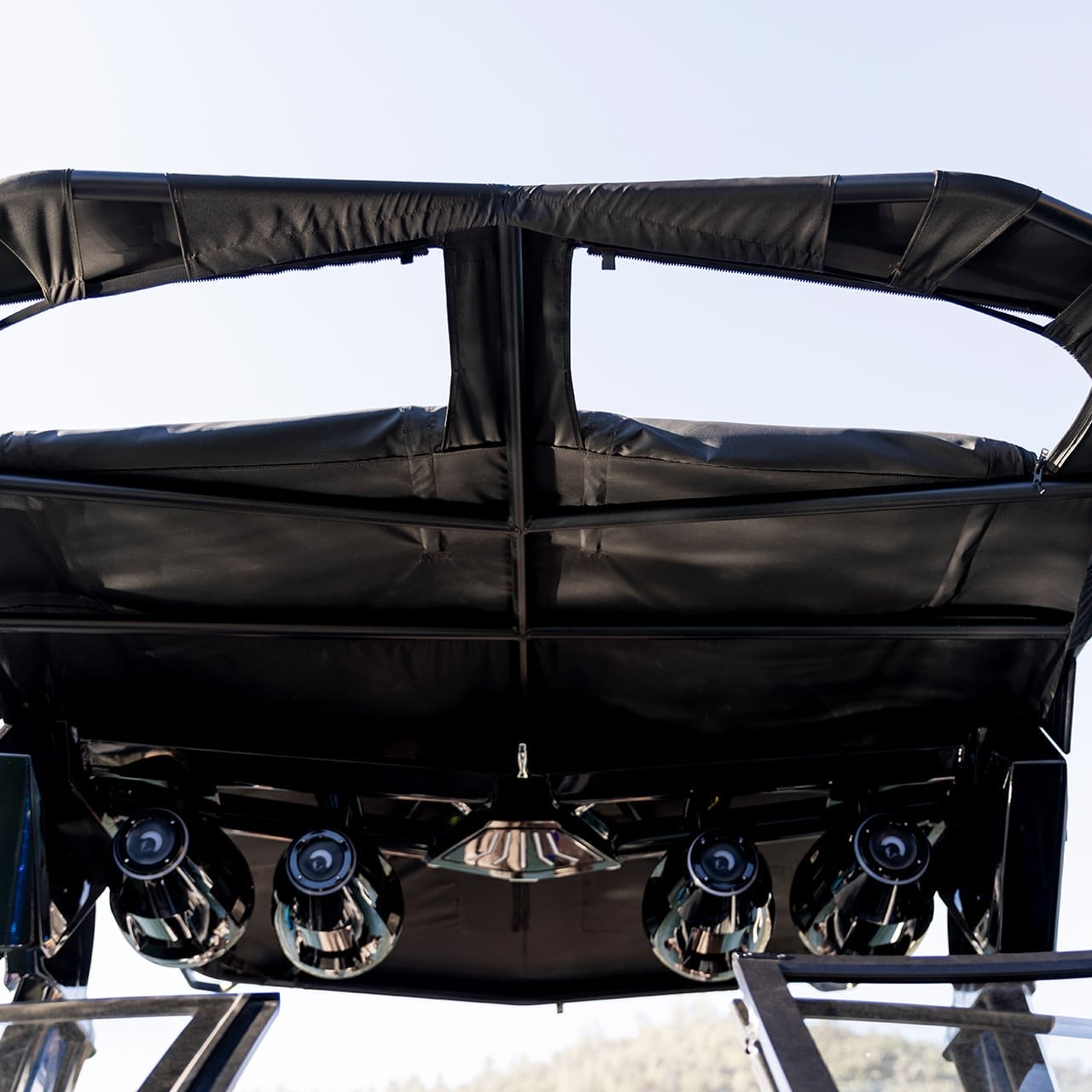 Close-up of a black audio system with speakers mounted under the canopy of a Centurion Ri230 boat, viewed from below against a clear sky.