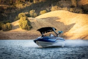 A Centurion Ri230 with a black canopy speeds across the lake, its sleek blue design contrasting against the backdrop of hills and trees.