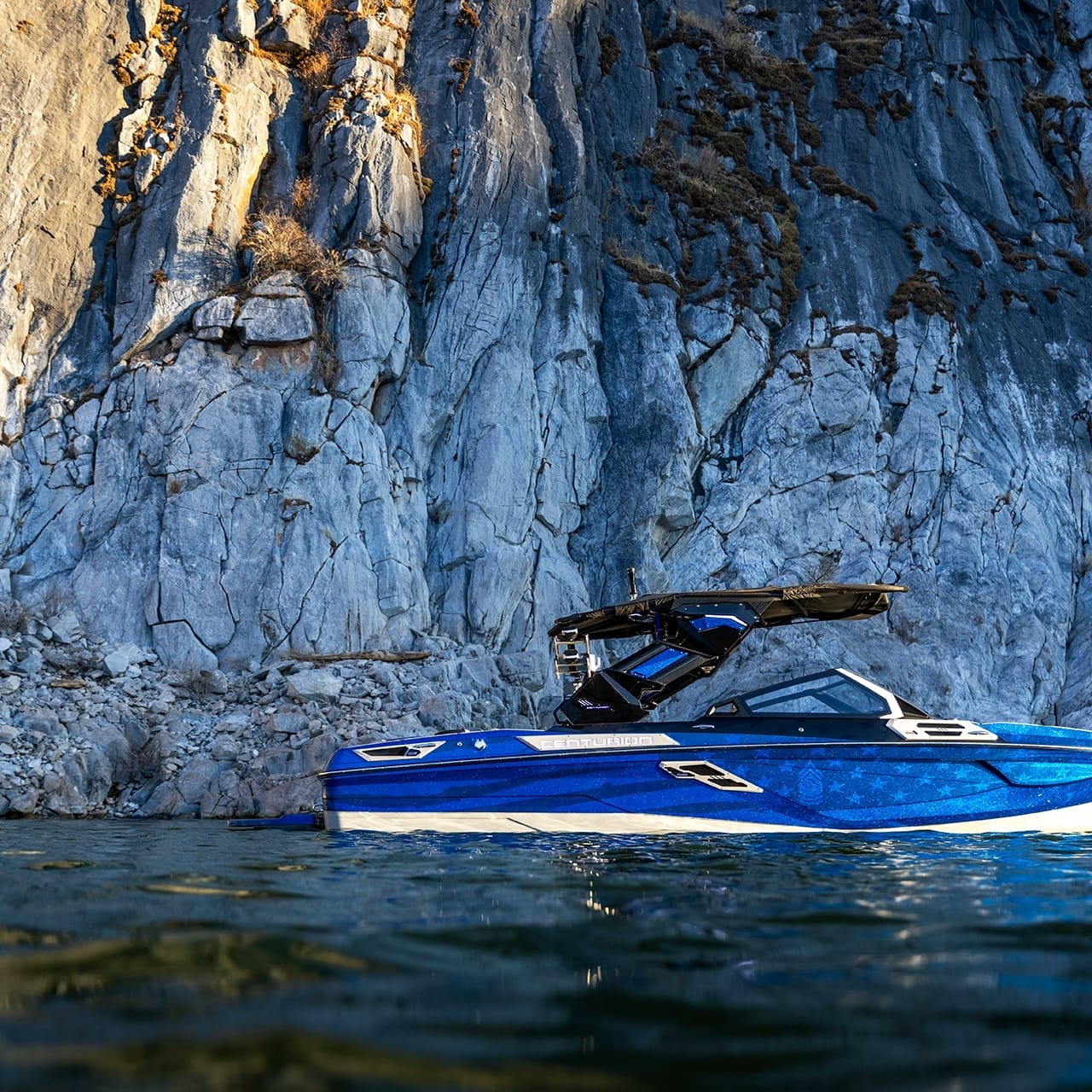 A blue Centurion Ri230 boat is gracefully floating on the water in front of a large rocky cliff.