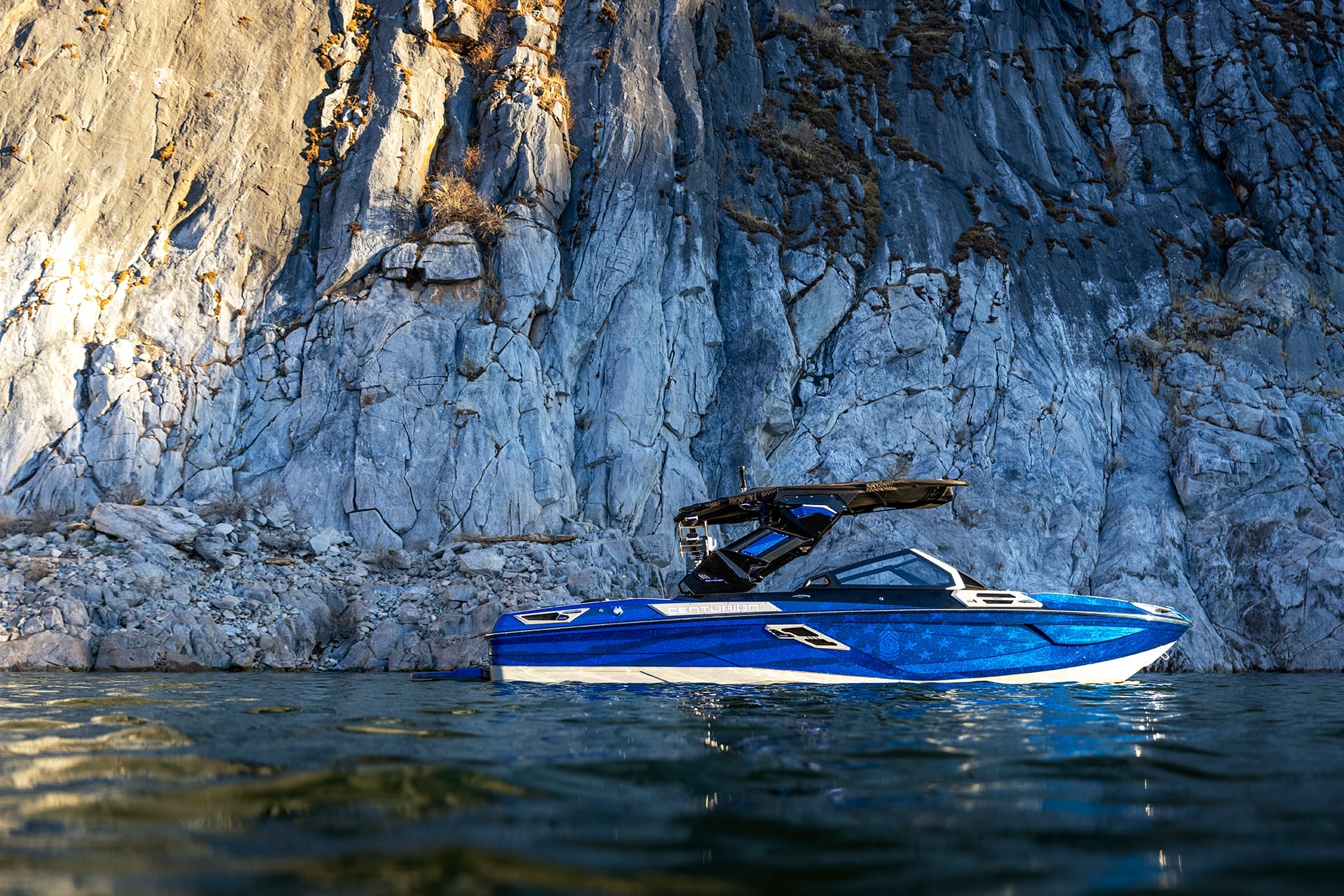 A blue Centurion Ri230 boat is gracefully floating on the water in front of a large rocky cliff.