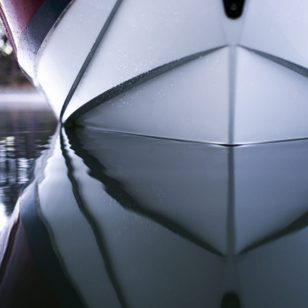 Close-up view of a Centurion Ri245's hull reflecting on calm water slightly misted, with the pointed bow of the boat featured prominently.