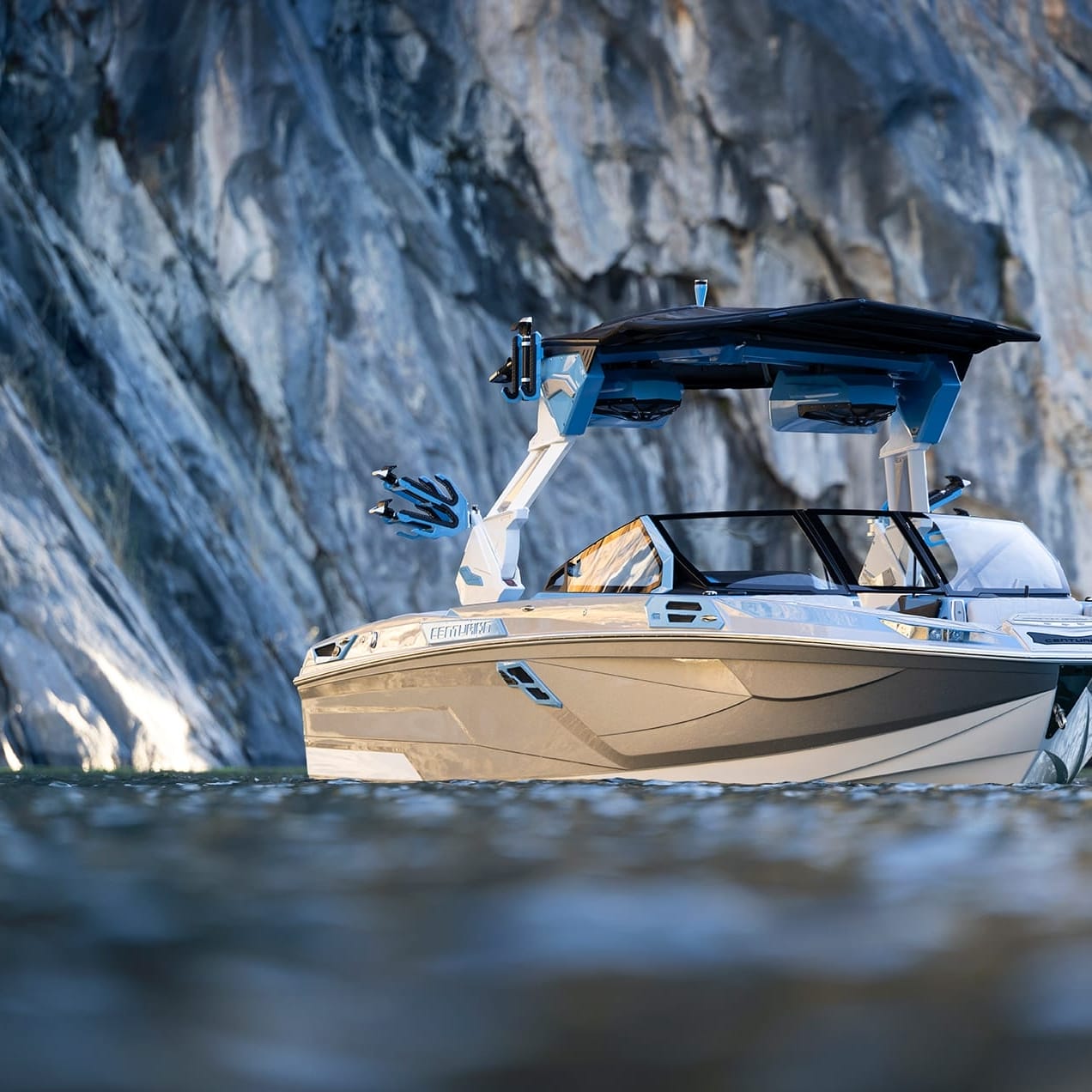 A Centurion Ri245 with a covered deck floats gracefully on calm water, framed by a rugged rocky cliff backdrop.