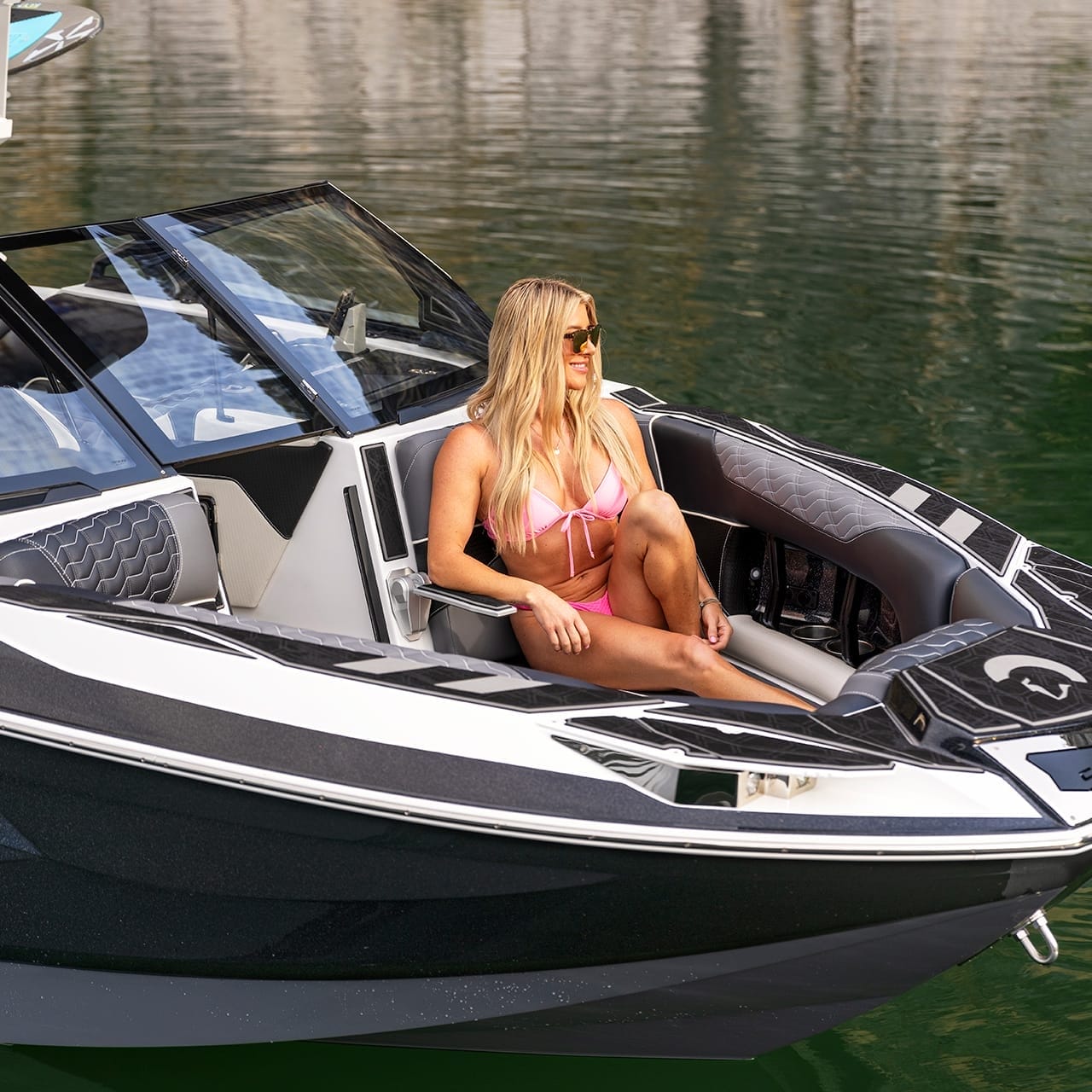 A person wearing a pink bikini sits in the bow of a sleek Centurion Ri265 on calm water, showcasing its modern design and black and white color scheme.