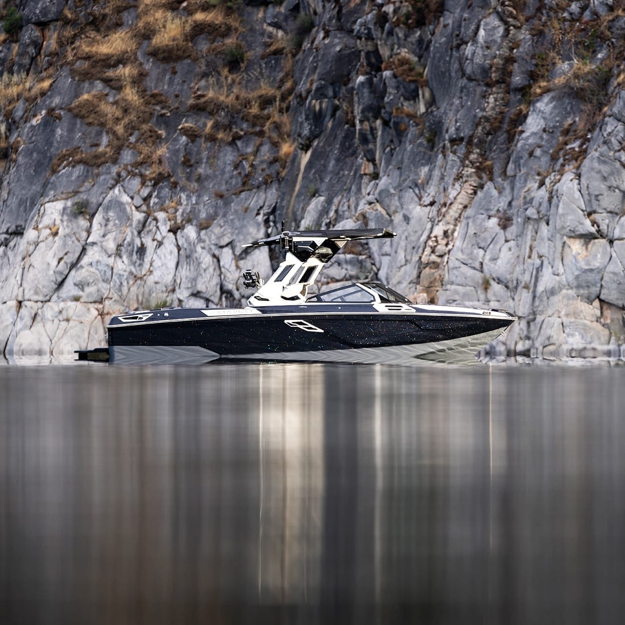 A Centurion Ri265 motorboat, stylish in black and white, sits stationary on calm water with rocky cliffs in the background.