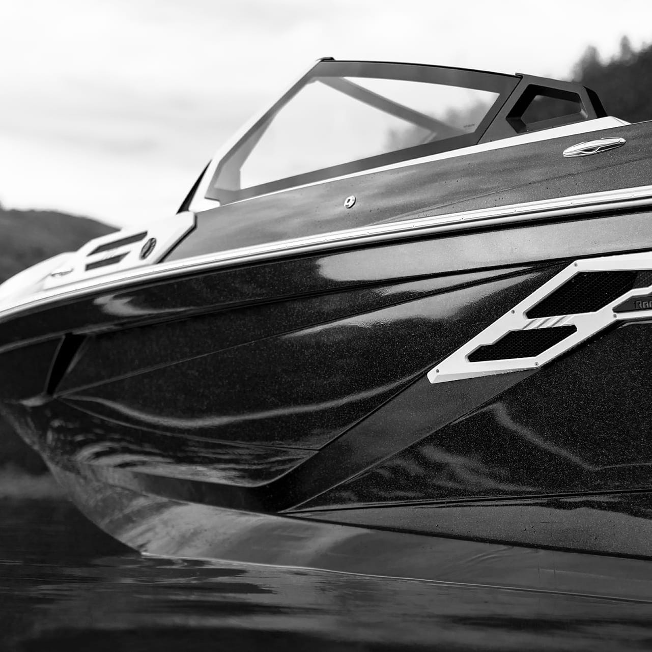 Black and white image of a sleek, modern Centurion Ri265 motorboat on water, showcasing its angled hull and partial cockpit with mountains in the background.