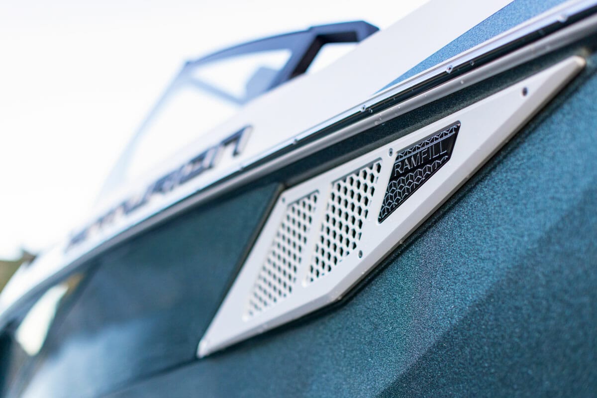 A close up of a blue and white wakesurf boat with a grill on the side.