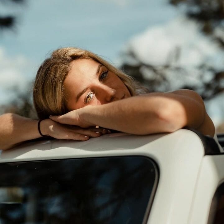 A woman leaning on the hood of a wakesurf boat.