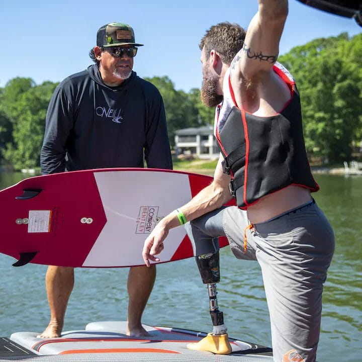 Two men standing on a boat with a wakesurf board.