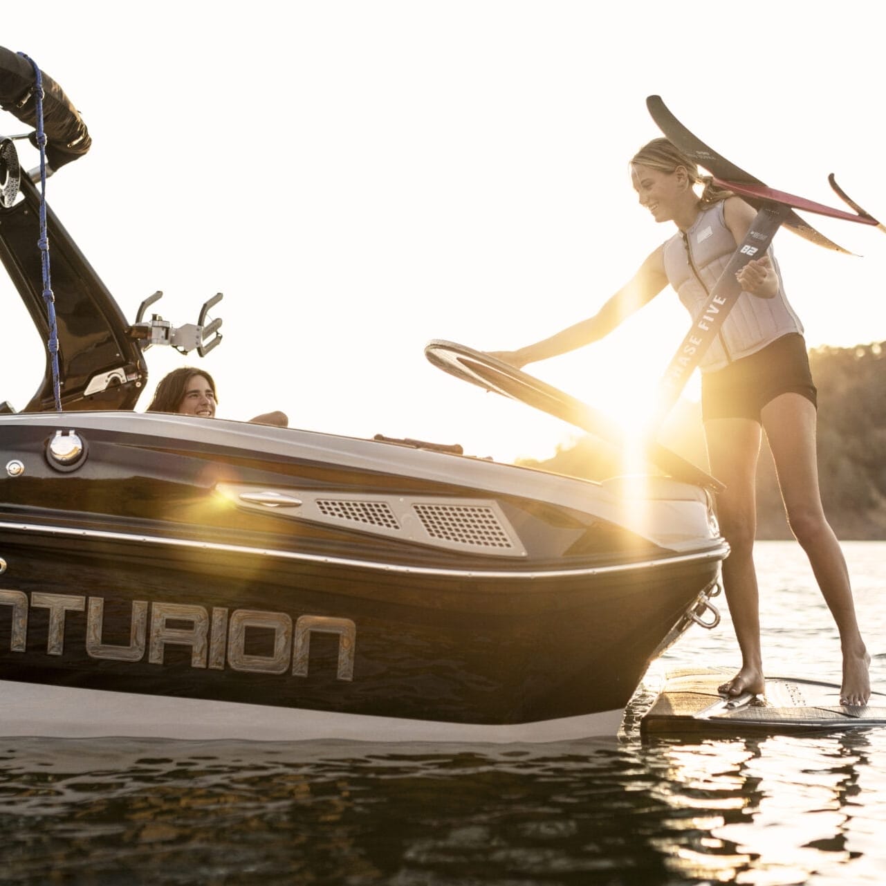 Kenzie Hickey gracefully steps onto a Centurion boat, clutching a water ski as the sun sets behind her.