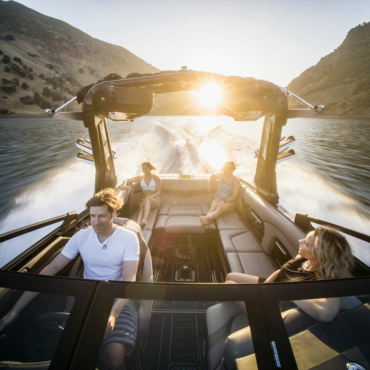 A group of people riding a wakesurf board behind a wakeboat on a lake.