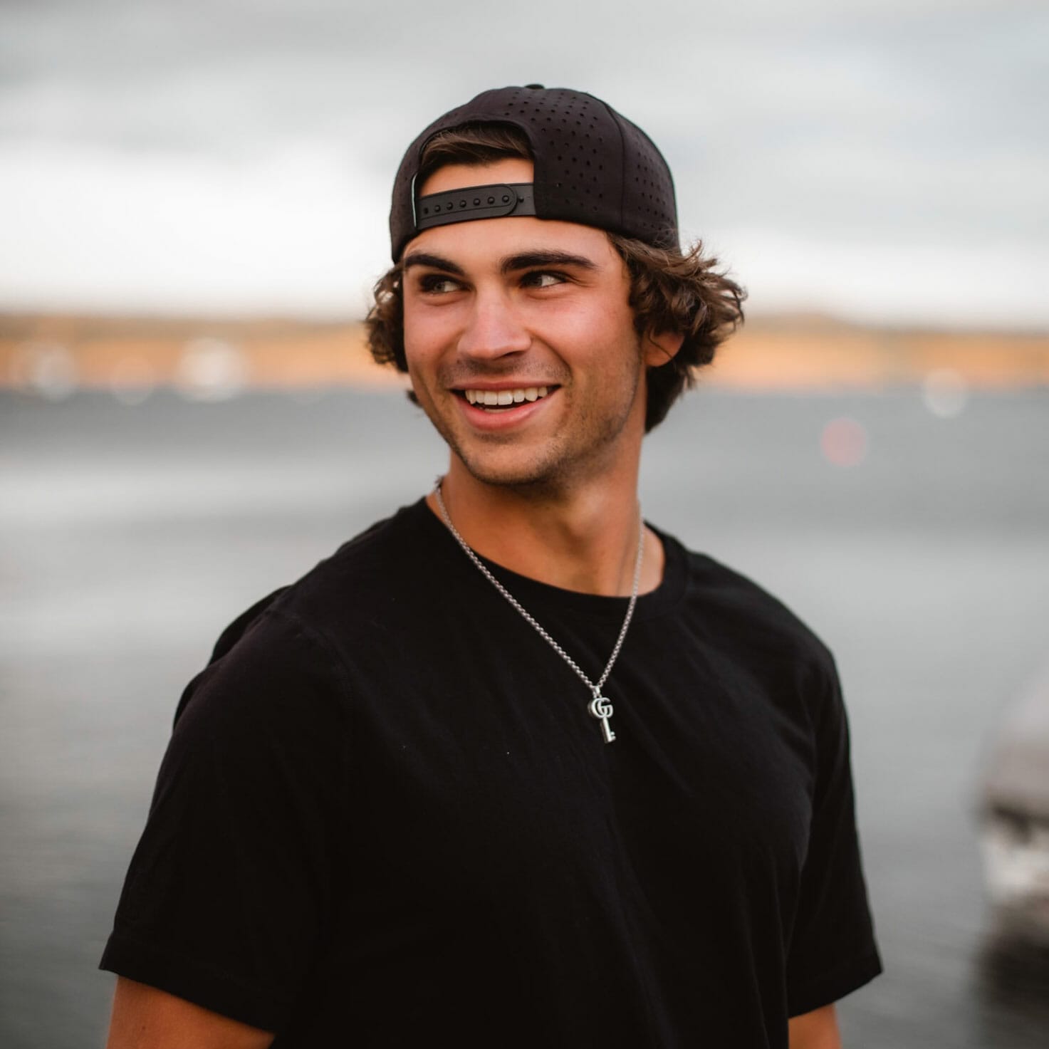 A young man wearing a black hat and a black shirt on a wakesurf boat.