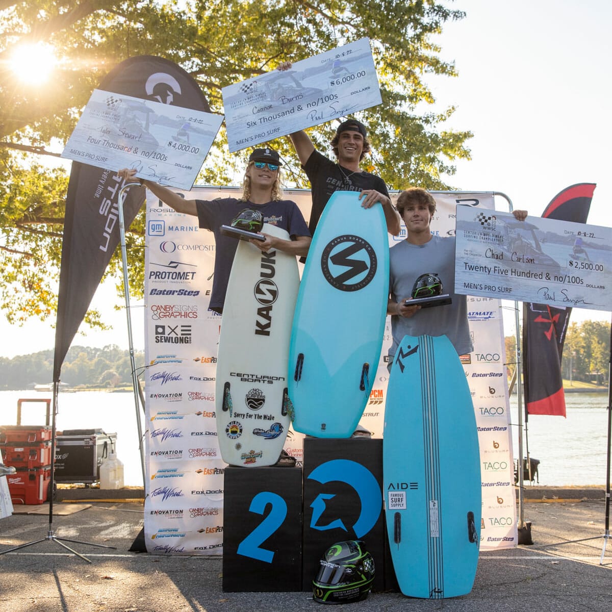 A group of people holding surfboards near a wakesurf boat.