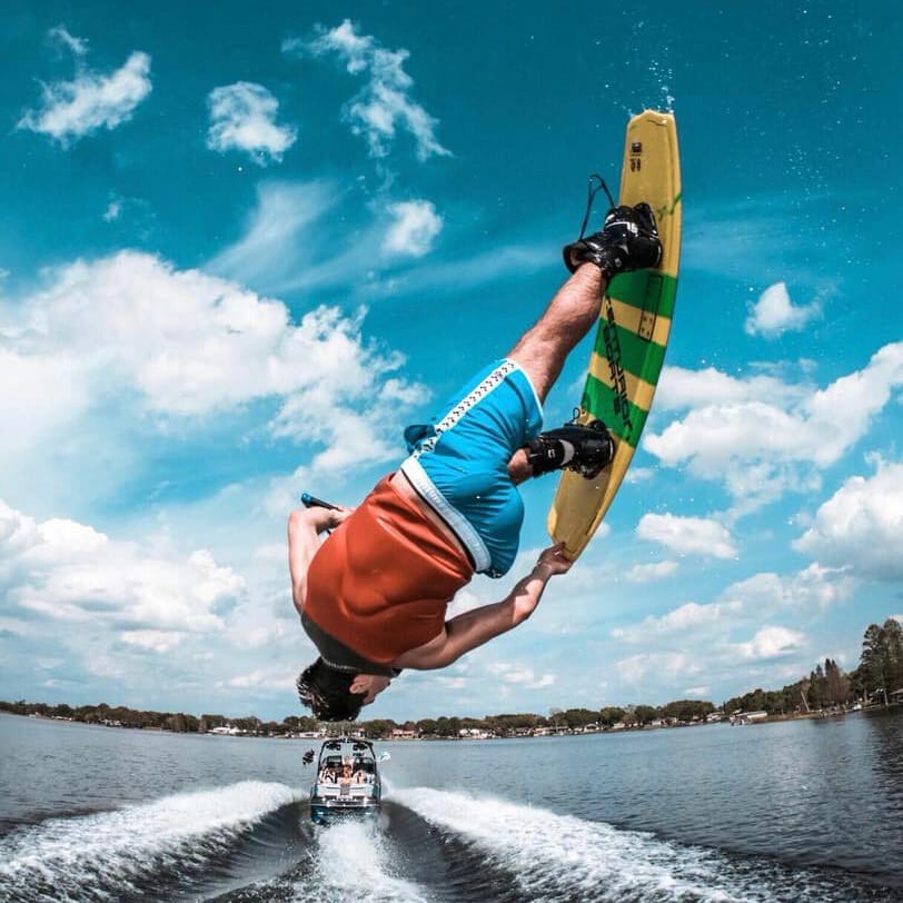 A man performing a trick on a wakesurf board behind a boat.