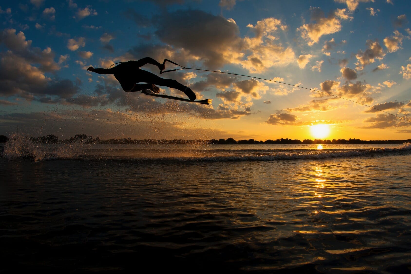 A person wakeboarding on a wakesurf board at sunset.