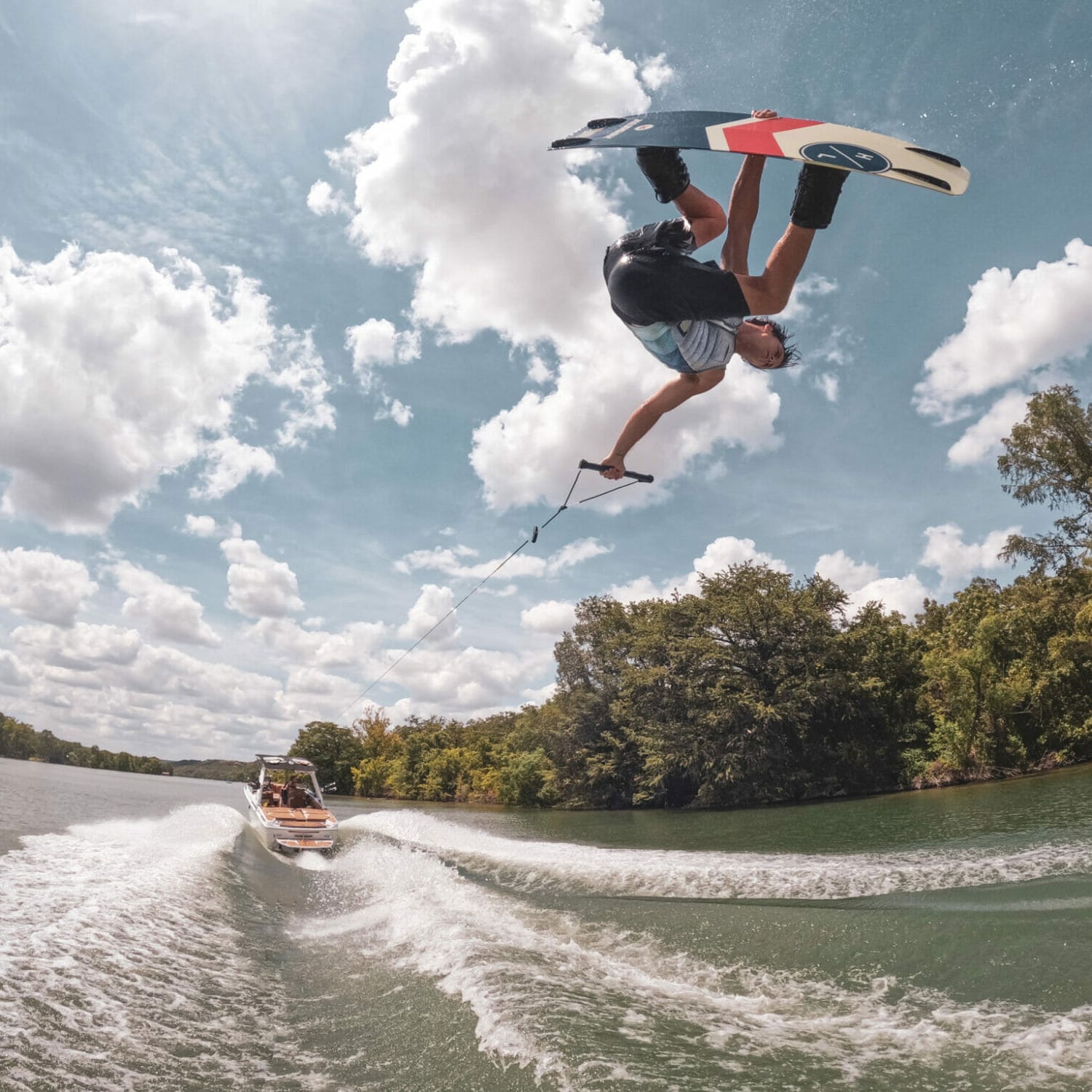 A man performing a trick on a wakeboard behind a wakeboat.