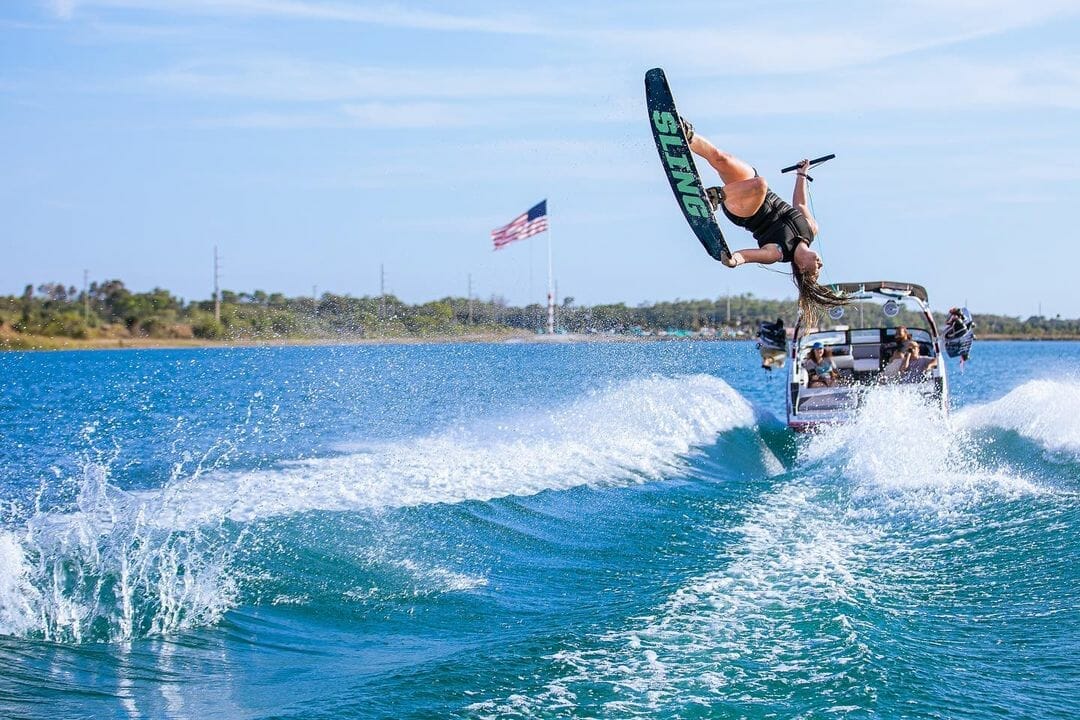 A person performing a wakeboard stunt behind a wakesurf boat.