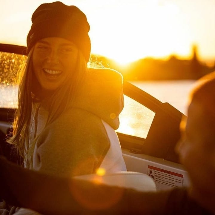 A man and woman are driving a wakesurf boat at sunset.