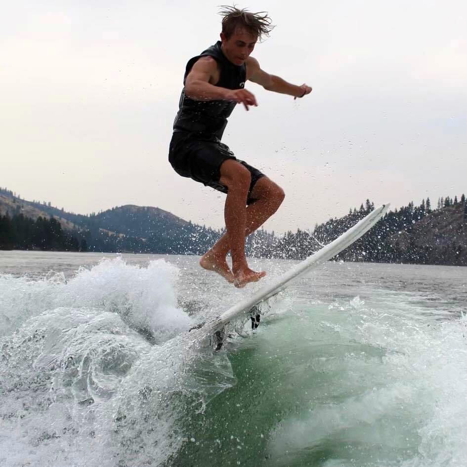 A man riding a wave on a wakesurf board.