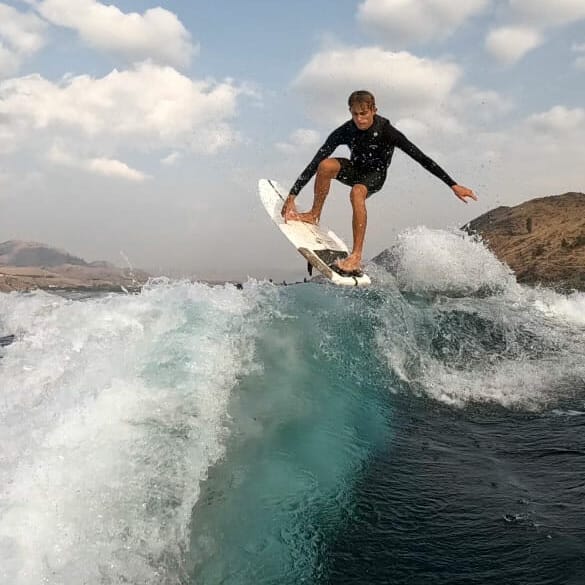 A man riding a wave on a wakesurf board.