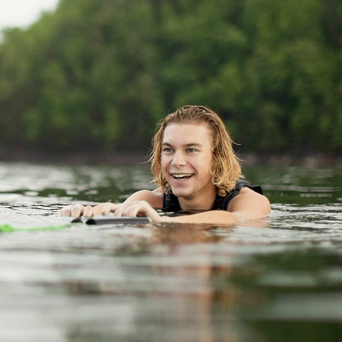 A young man is wakesurfing behind a boat.