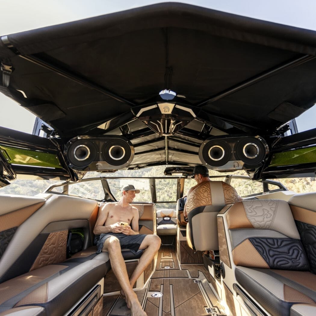 A man is sitting in the back of a wakesurf boat.