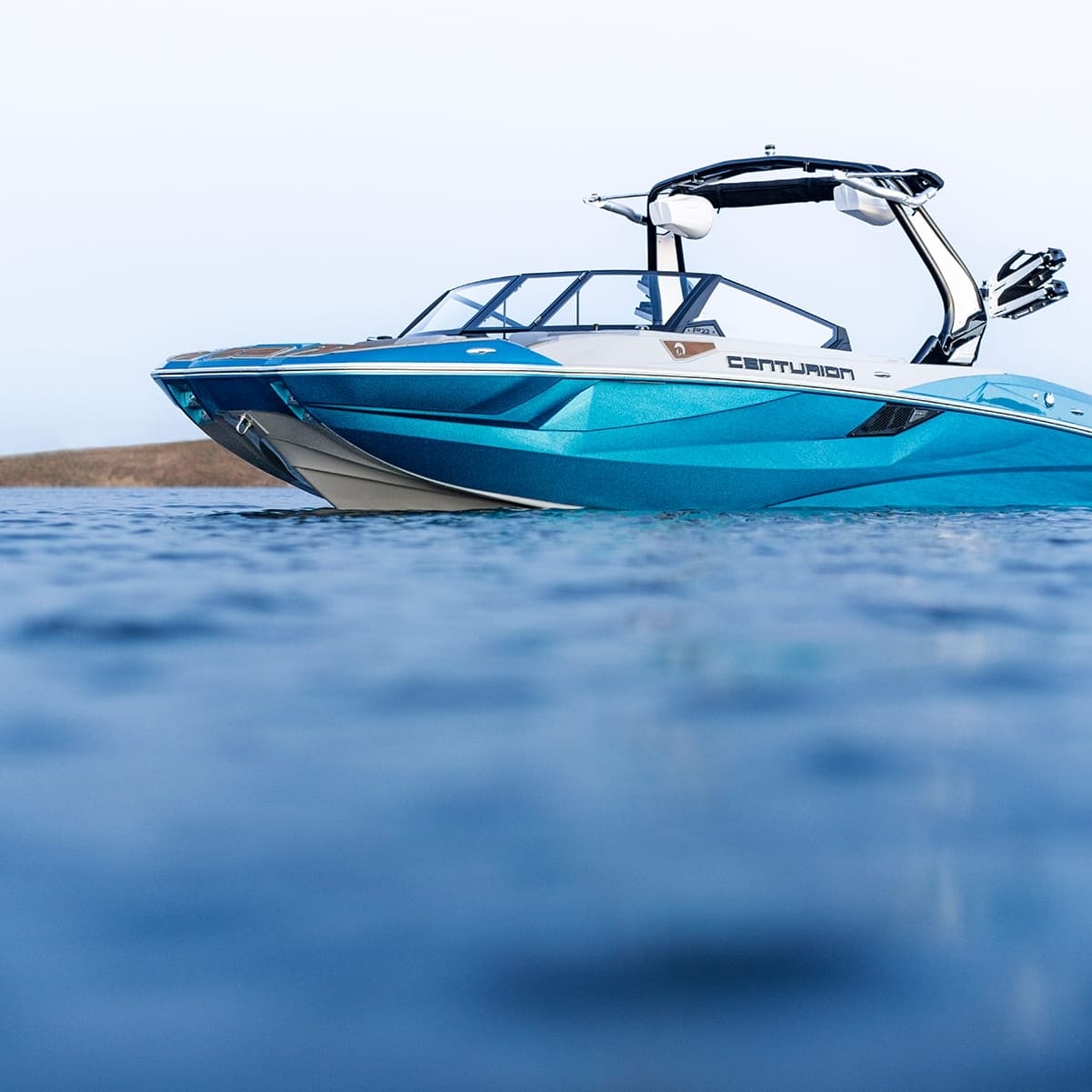 A blue and white Centurion Fe22 boat floats on a calm body of water with hills visible in the background.