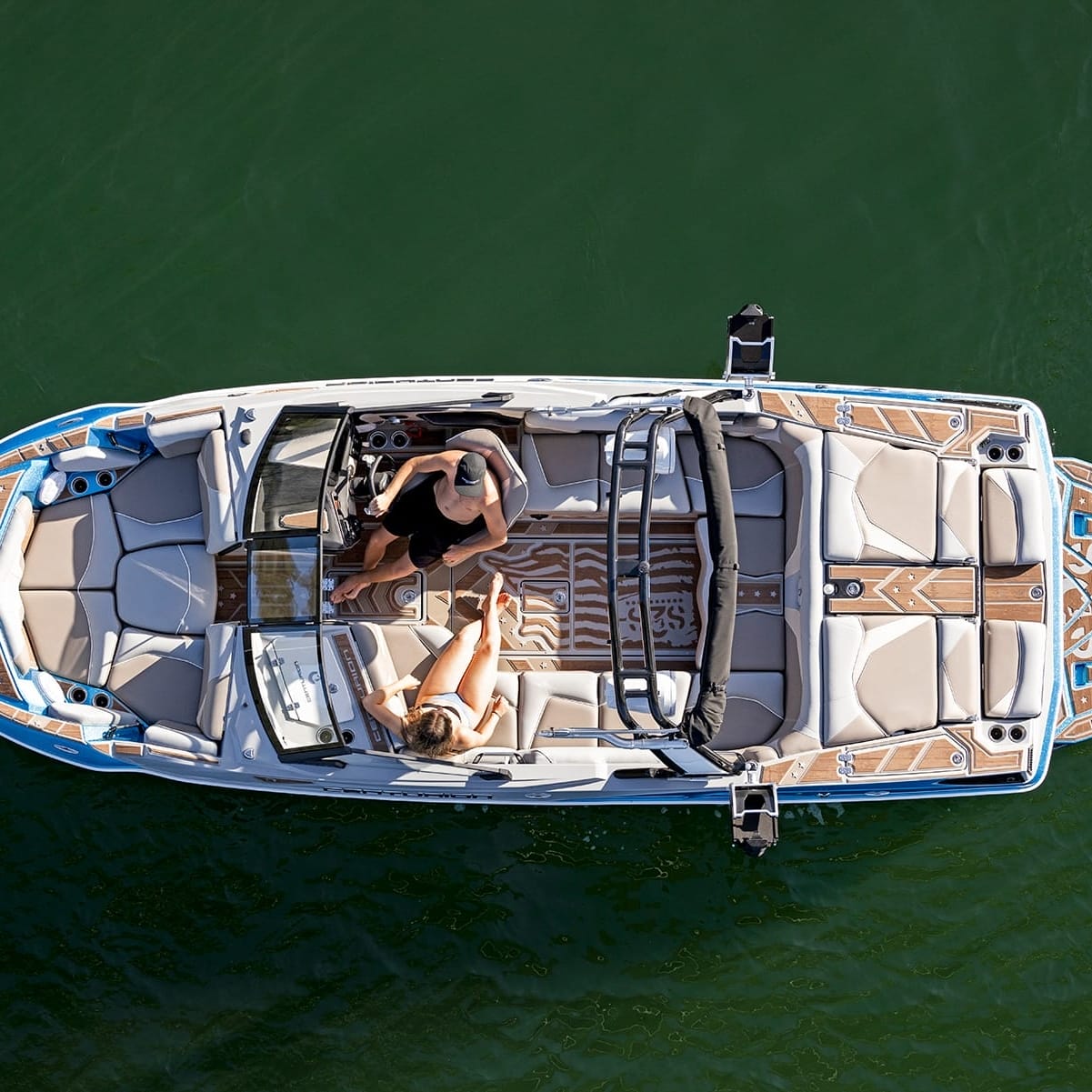 Aerial view of two people sitting on a sleek, modern Centurion Fe22 motorboat with detailed seating and design, floating on a green-colored lake.