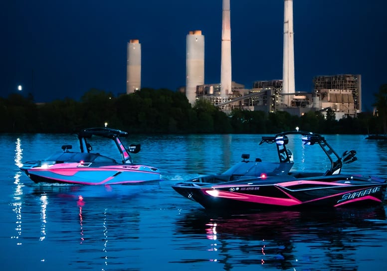 Two pink boats in the water at night near a power plant.