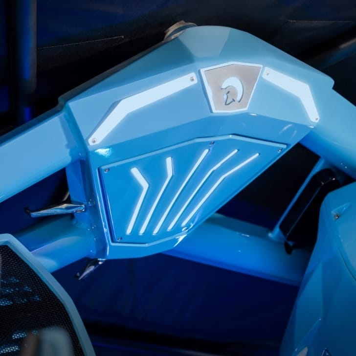 Close-up of a blue mechanical structure with illuminated light accents and a metallic emblem featuring a stylized helmet design.