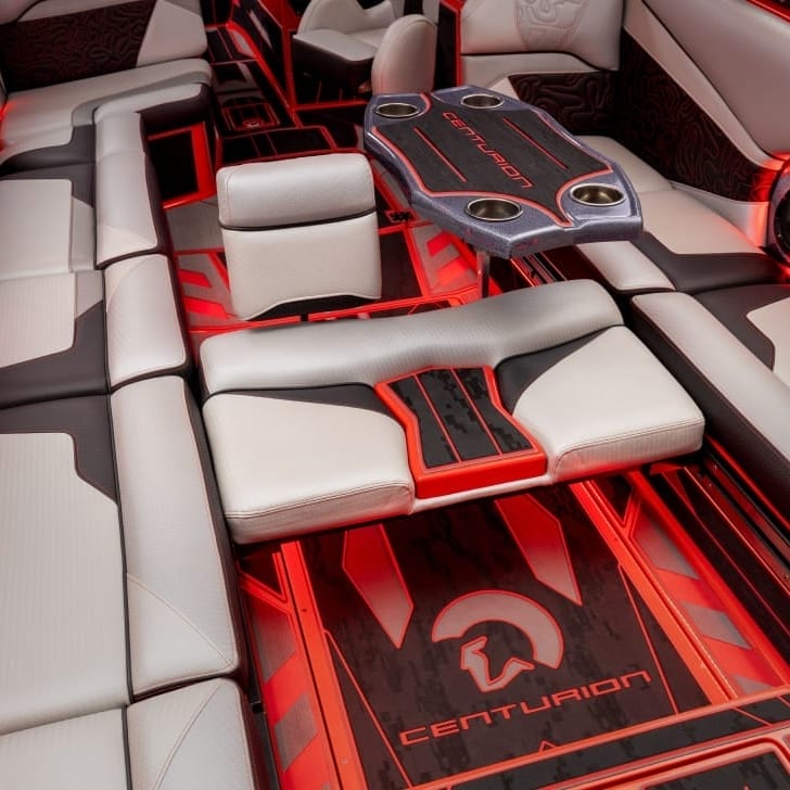 An interior view of a luxury boat with white and black cushioned seats, a Centurion logo, and red accent lighting.