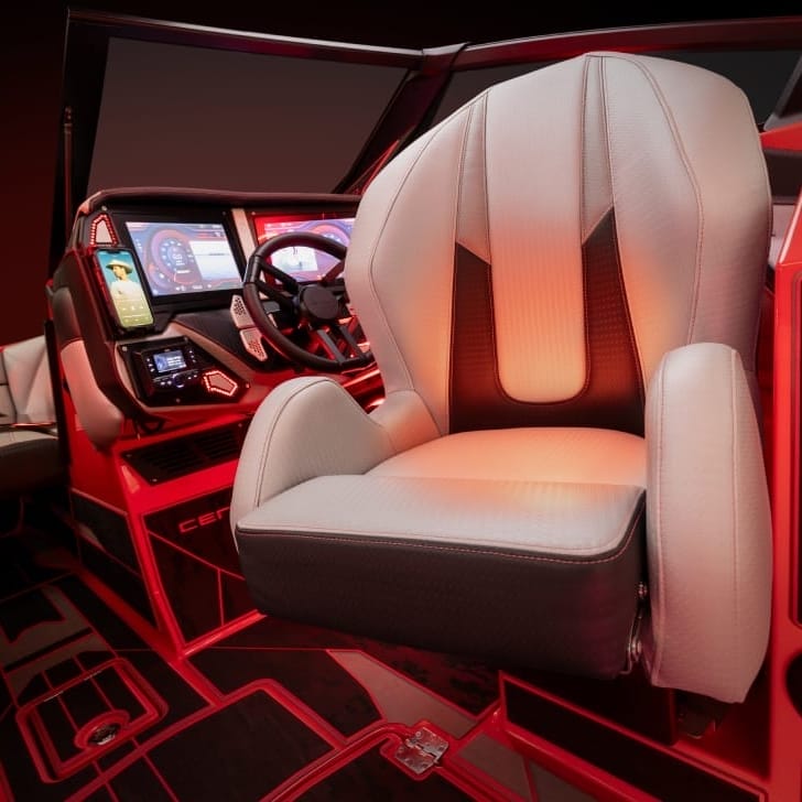 A modern, illuminated boat or yacht cockpit with a cushioned captain's chair, multiple digital displays, and a smartphone mount. The scene is lit with a red ambient light.