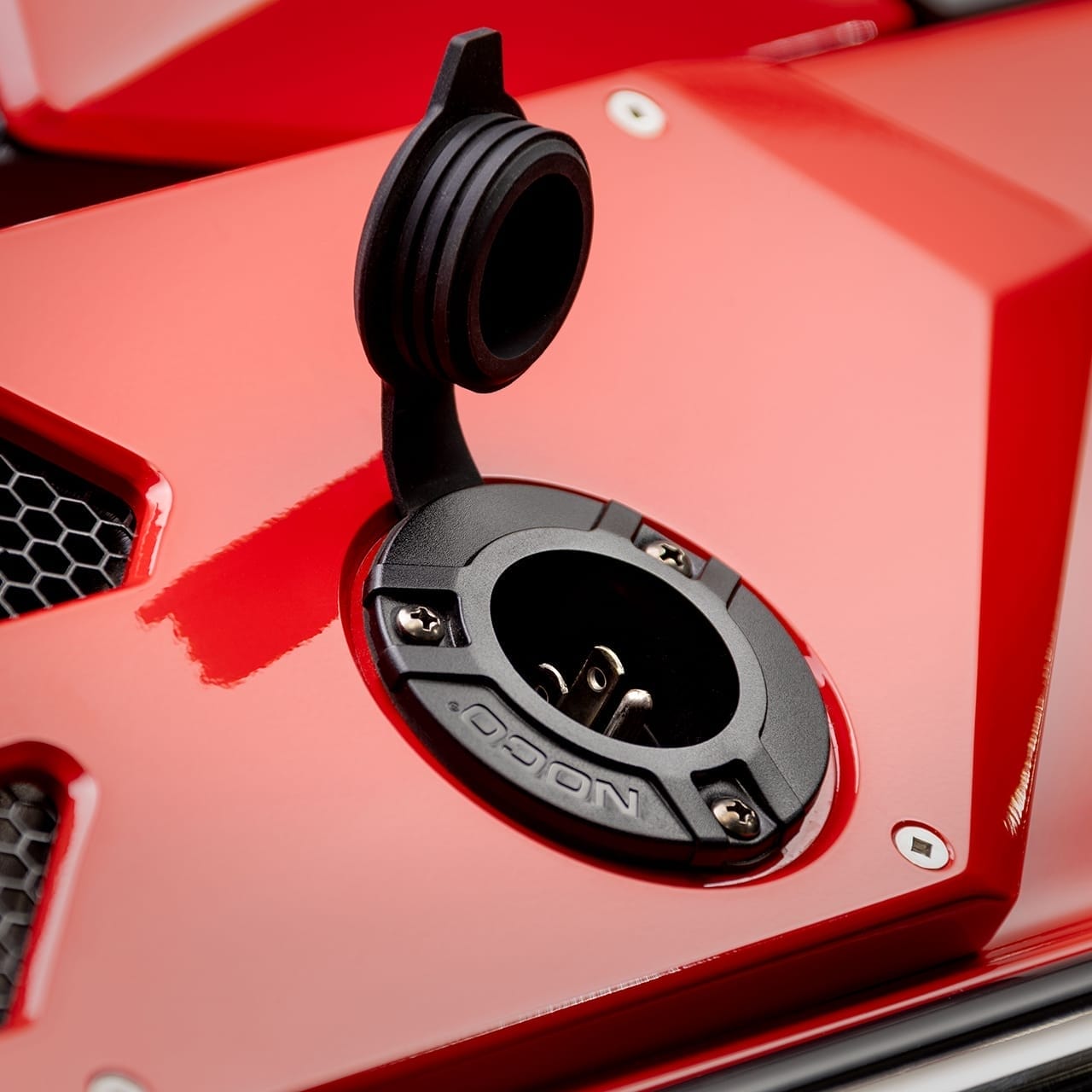 Close-up of an open charging port on the sleek, red exterior of a modern vehicle with black detailing.