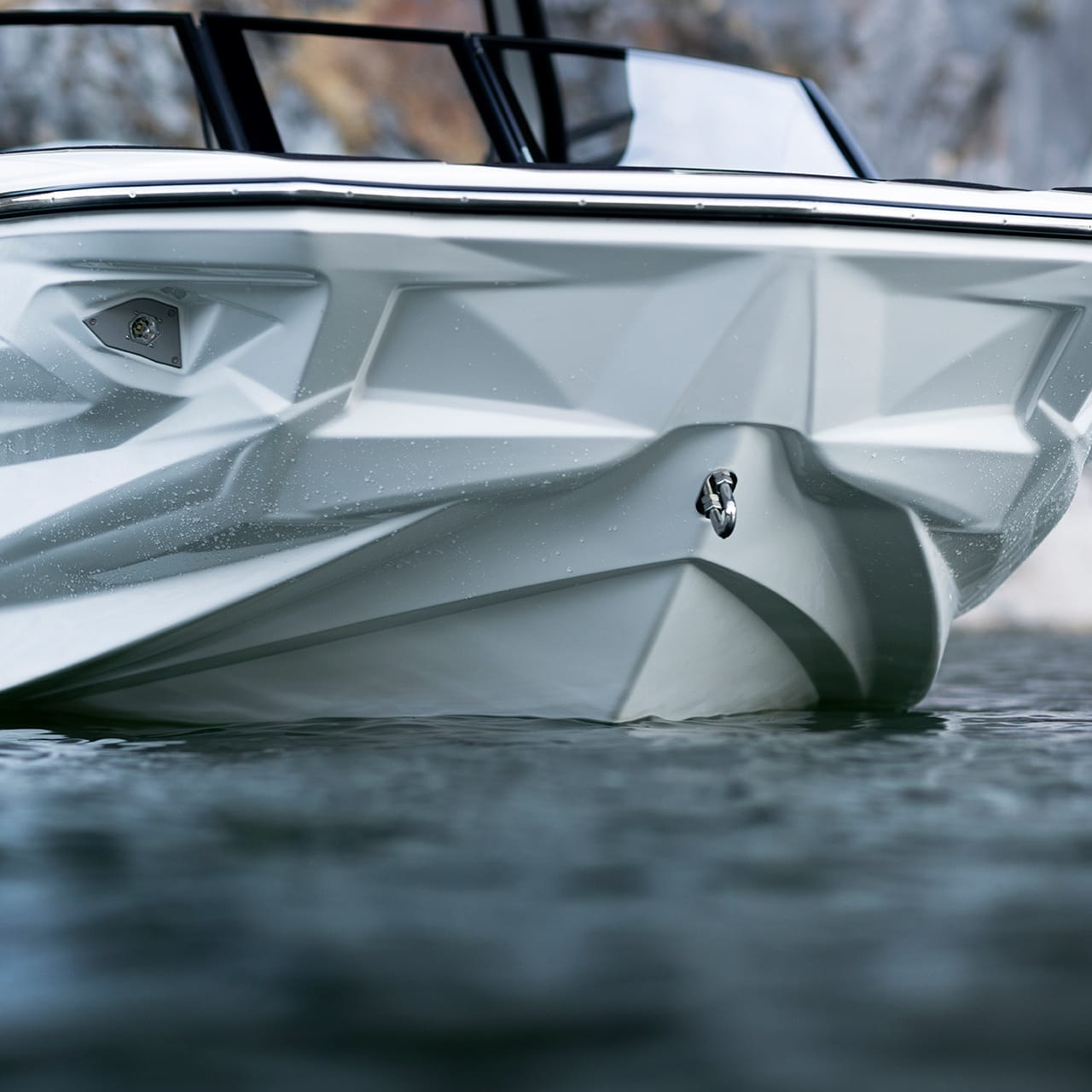 Close-up of a sleek Centurion Fe Series boat's bow floating on water, with a rocky shoreline in the background.