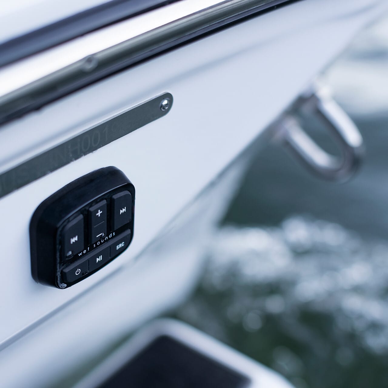 Close-up of a Centurion Fe Series boat's side reveals a sleek, black control panel with buttons for music playback. The shimmering ocean water provides a stunning backdrop.