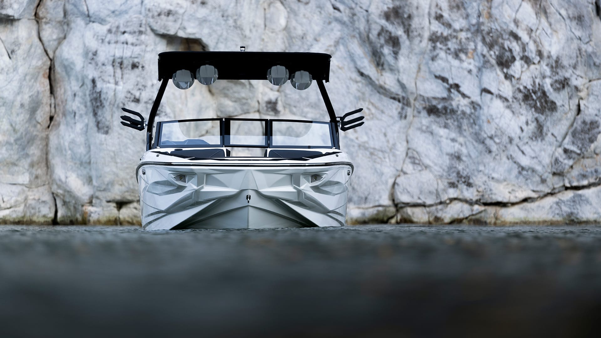 A sleek Centurion Fe Series speedboat with a black canopy is positioned in front of a large, textured rock wall on calm water.