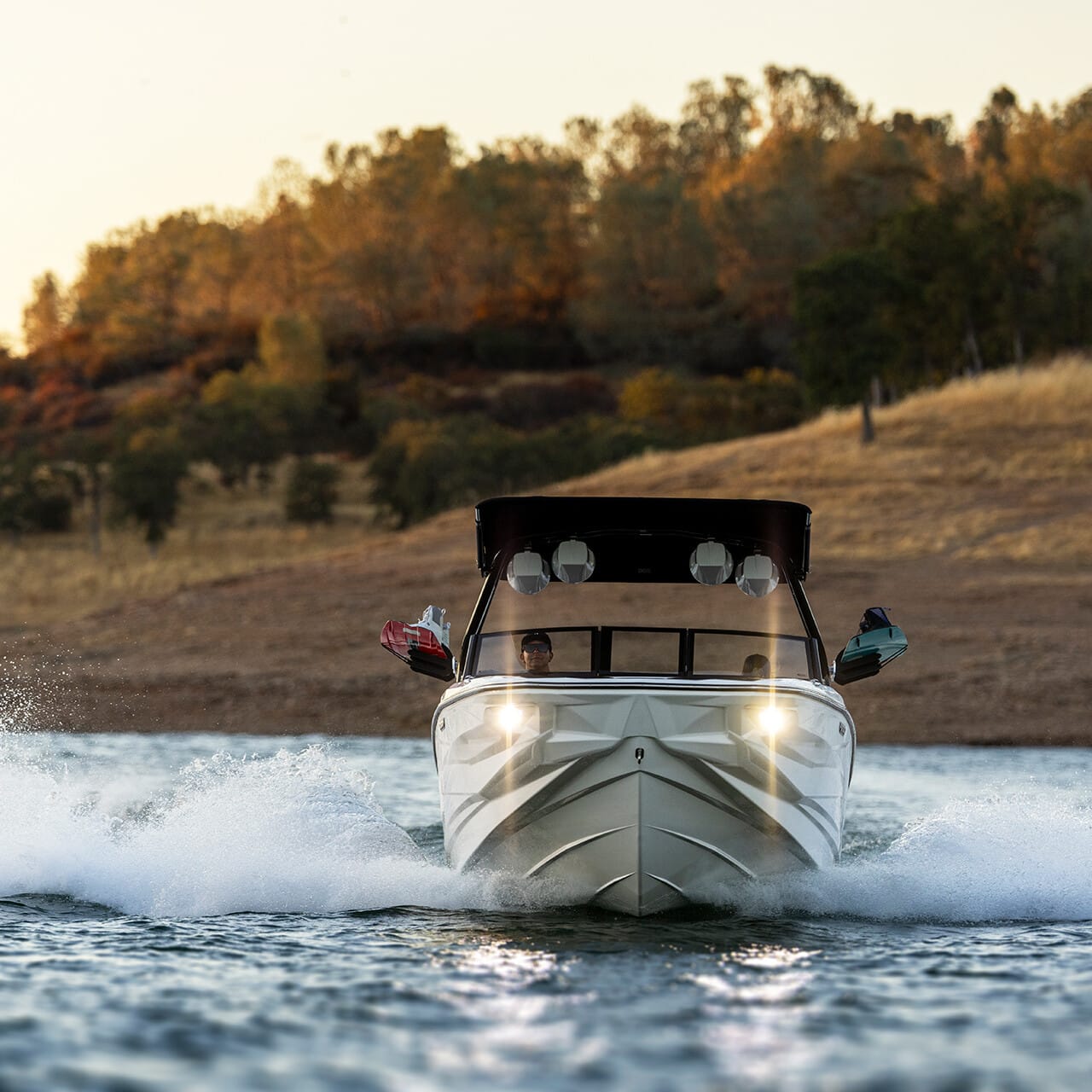 A Centurion Fe Series motorboat with lights on speeds across the lake, creating splashes. Trees and a hilly shore are visible in the background.