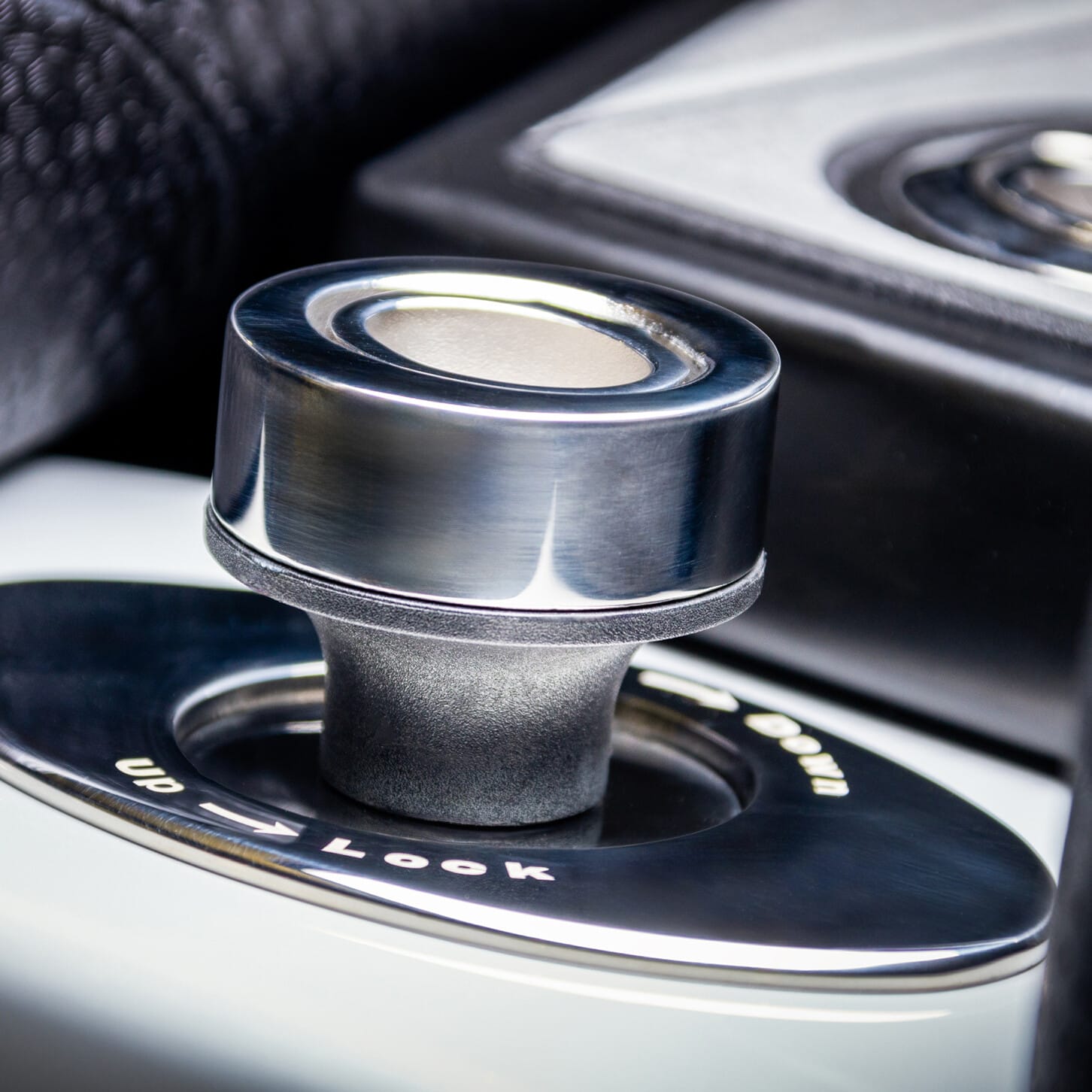 Close-up of a car's gear selector knob with metallic finish, surrounded by textured black material.